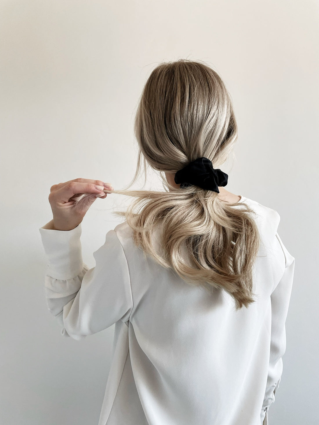 Blonde girl from the back, wearing a white blazer and black silk scrunchie in her wavy hair