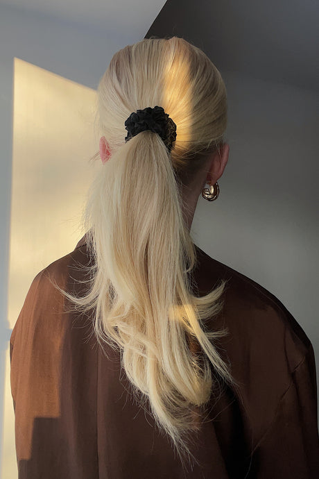 Blond girl wearing a black silk scrunchie in her beautiful ponytail, sun shining on her hair