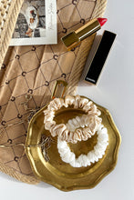 Load image into Gallery viewer,  Beige and white natural silk scrunchies on a golden plate next to an open purse and red lipstick
