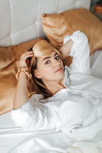 A young woman lying in bed, just waking up, wearing a luxurious silk sleep mask.