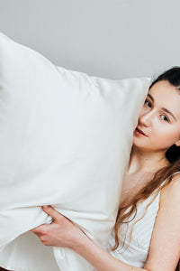 A dark haired girl holding white silk pillowcase gently