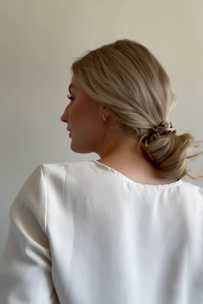 Blond girl making a stylish low messy bun with beige silk scrunchie