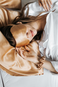 Cozy beauty sleep: a girl, still in bed, with a natural silk sleep mask in gold colour embracing her eyes.