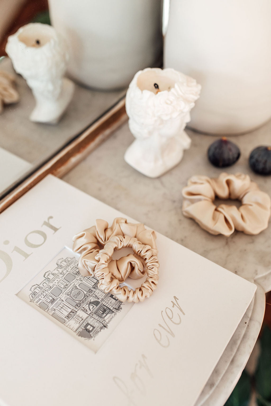 Marble vanity table with a candle beige silk scrunchies and a white Dior book on it