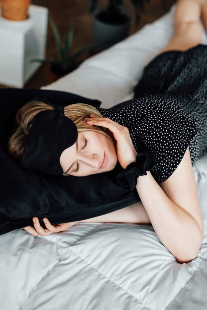 Content girl resting on black silk pillowcase, silk eye mask pushed back on her forehead