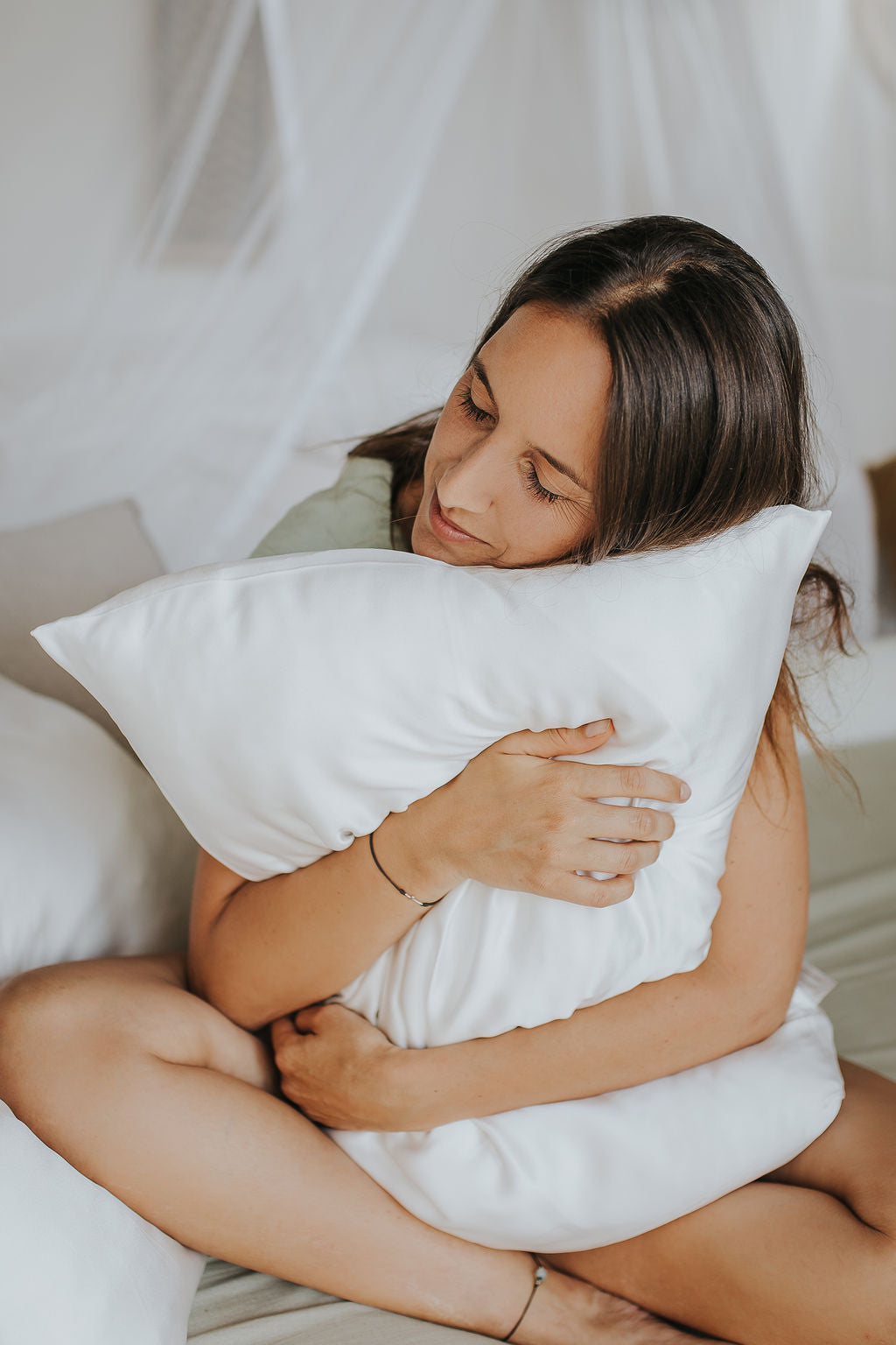 A girl gently hugs her white silk pillowcase