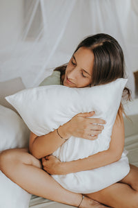 Dark haired, beautiful and dreamy girl snuggles with a white silk pillowcase.