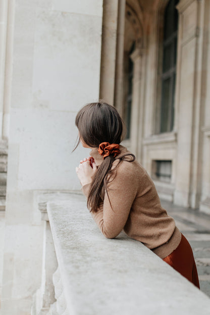 Girl in a cashmere sweater and silk skirt stopping to look over beautiful Paris, she has a cinnamon colour silk scrunchie in her dark hair