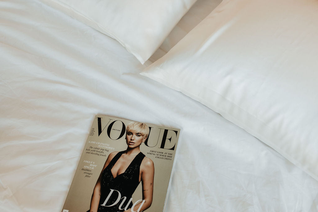 Minimalist bedroom with two white silk pillowcases and a Vogue lying on the bed