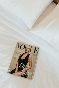 Divas baltas zīda spilvendrānas viesnīcas numuriņa guļamistabā ar Vogue žurnālu uz gultas